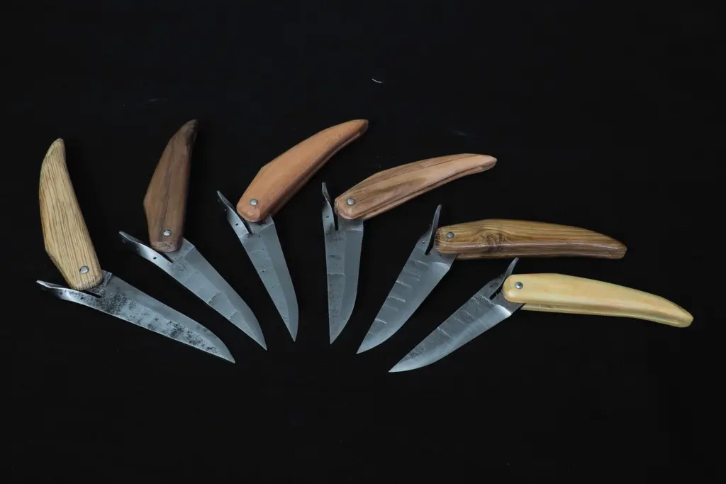 Seven Barachin knives open and fanned out on a black background, with handles in light and dark woods