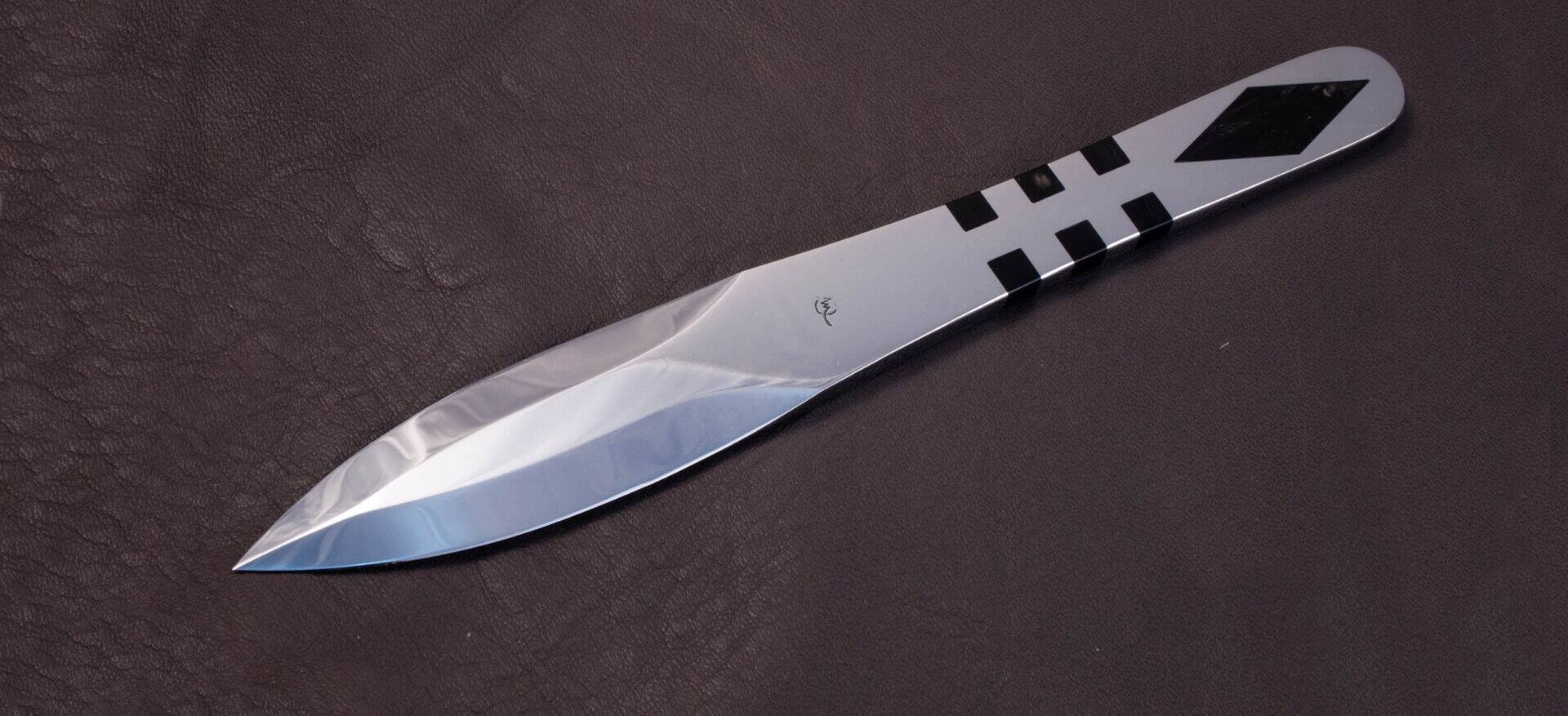 Mirror-polished throwing knife with black horn inserts on the grip, resting on leather