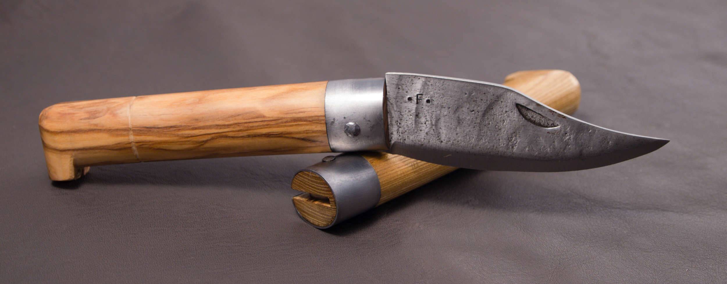 An open Frabosan with a pale grained wood handle resting on a closed Frabosan, with the metal ferrule at the base of the blade