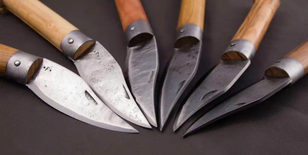 Close-up of six hand-forged Frabosan blades, with the hammered surface and the maker's stamp on the heel