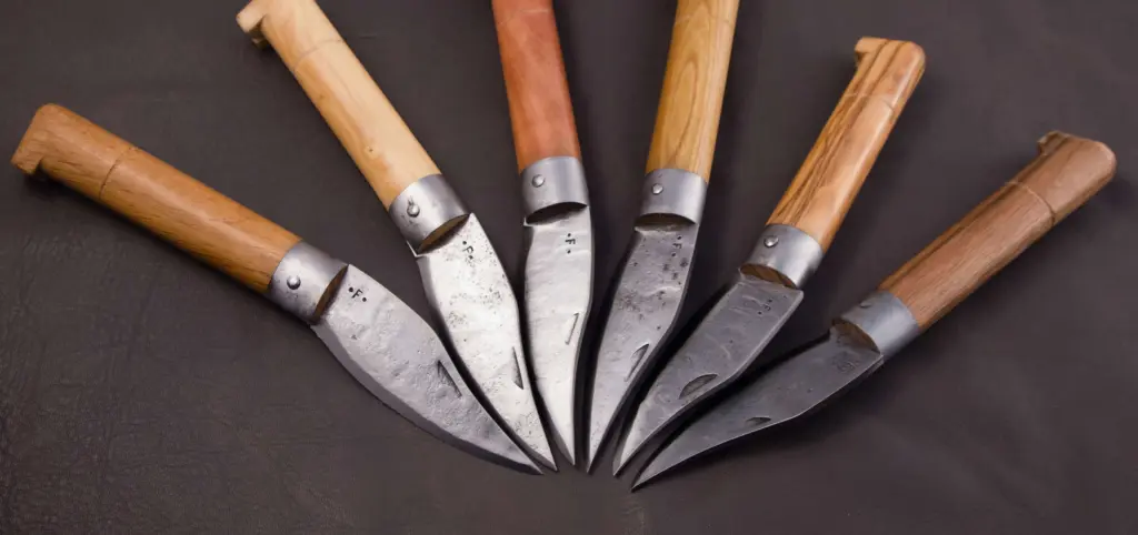Six Frabosan knives open and fanned out, seen from above, with handles in light and dark woods and the metal ferrule on each
