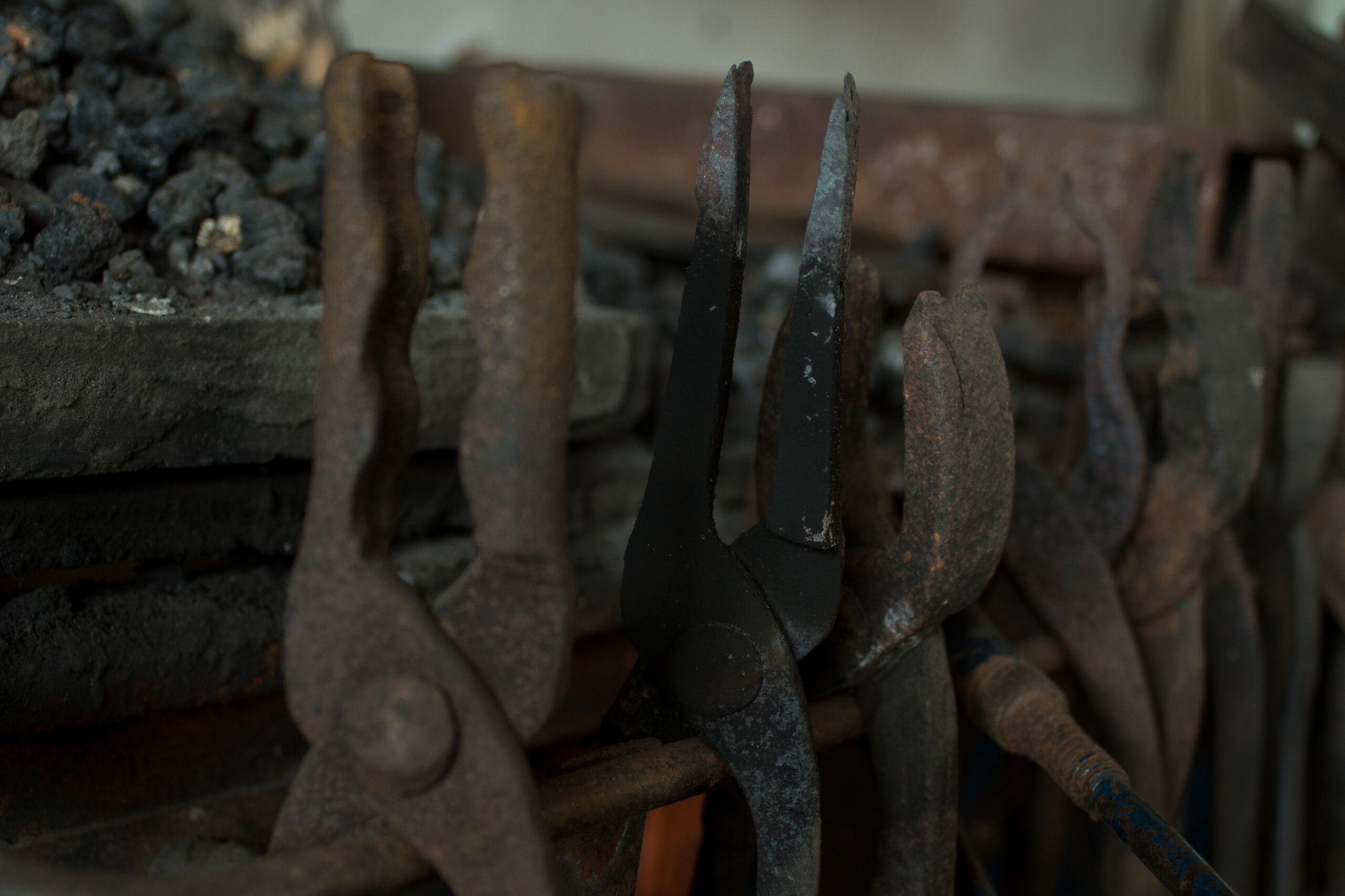 Forge tongs hanging in the workshop, beside the coal