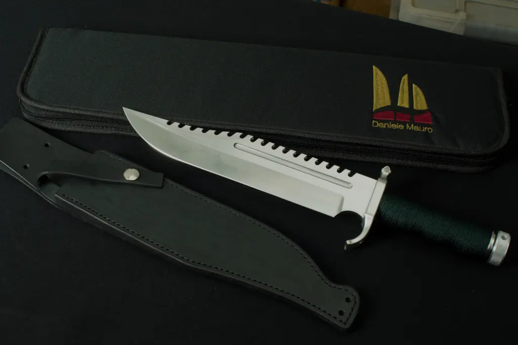 Replica of Gil Hibben's Rescue, green cord handle and sawback blade, beside the black leather sheath